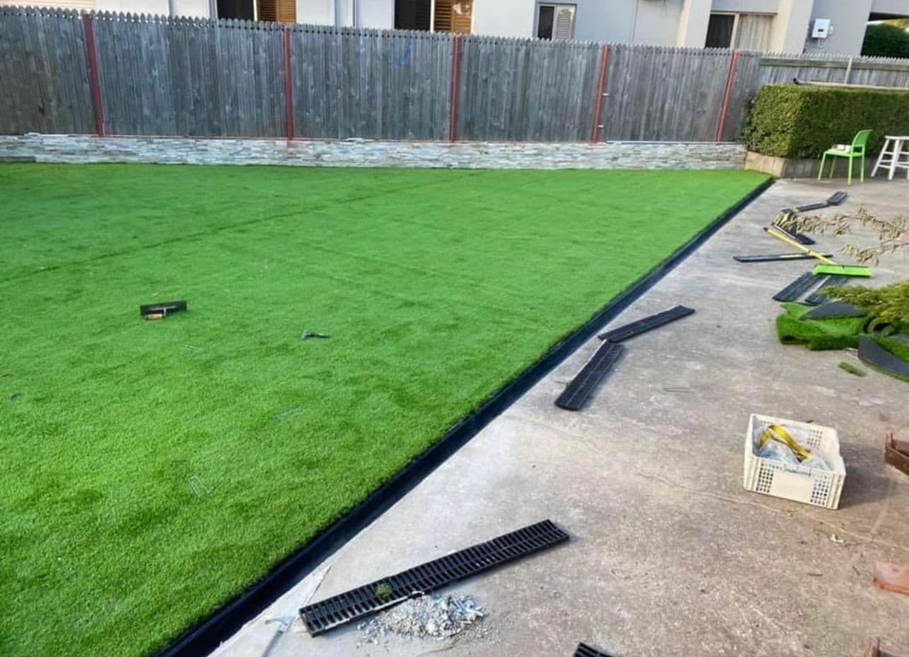 Artificial turf being laid and edged against a concrete path in a backyard