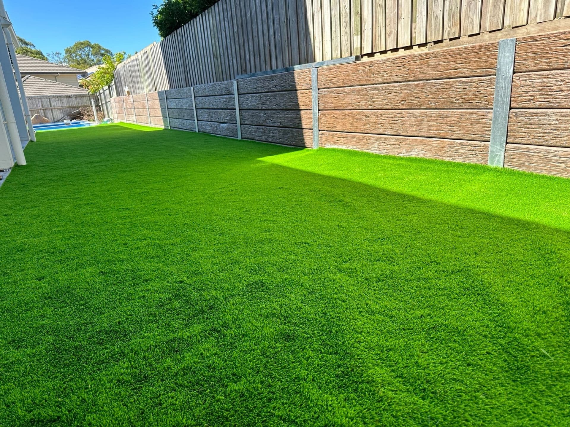Finished artificial turf lawn beside a timber sleeper retaining wall and paling fence