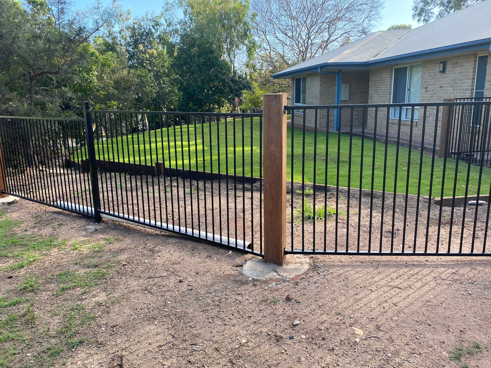 Black aluminium fence with a double gate and timber posts beside a lawn