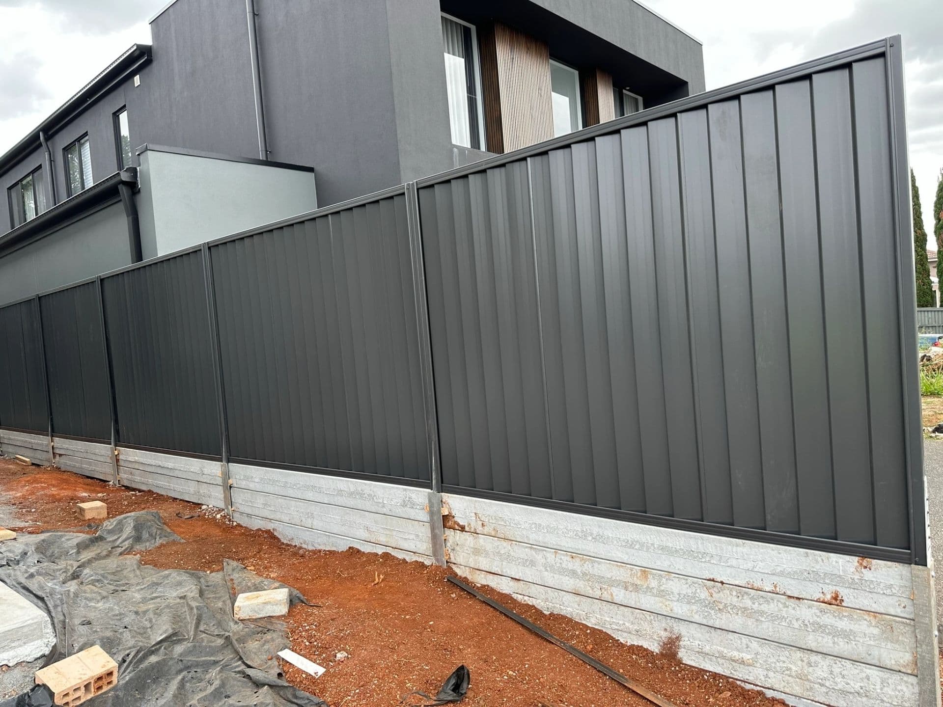 Dark Colorbond boundary fence on a concrete sleeper retaining wall at a new home