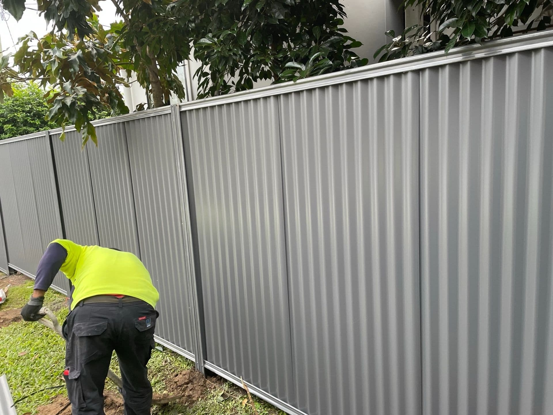 Landscaper installing grey Colorbond fence panels along a boundary